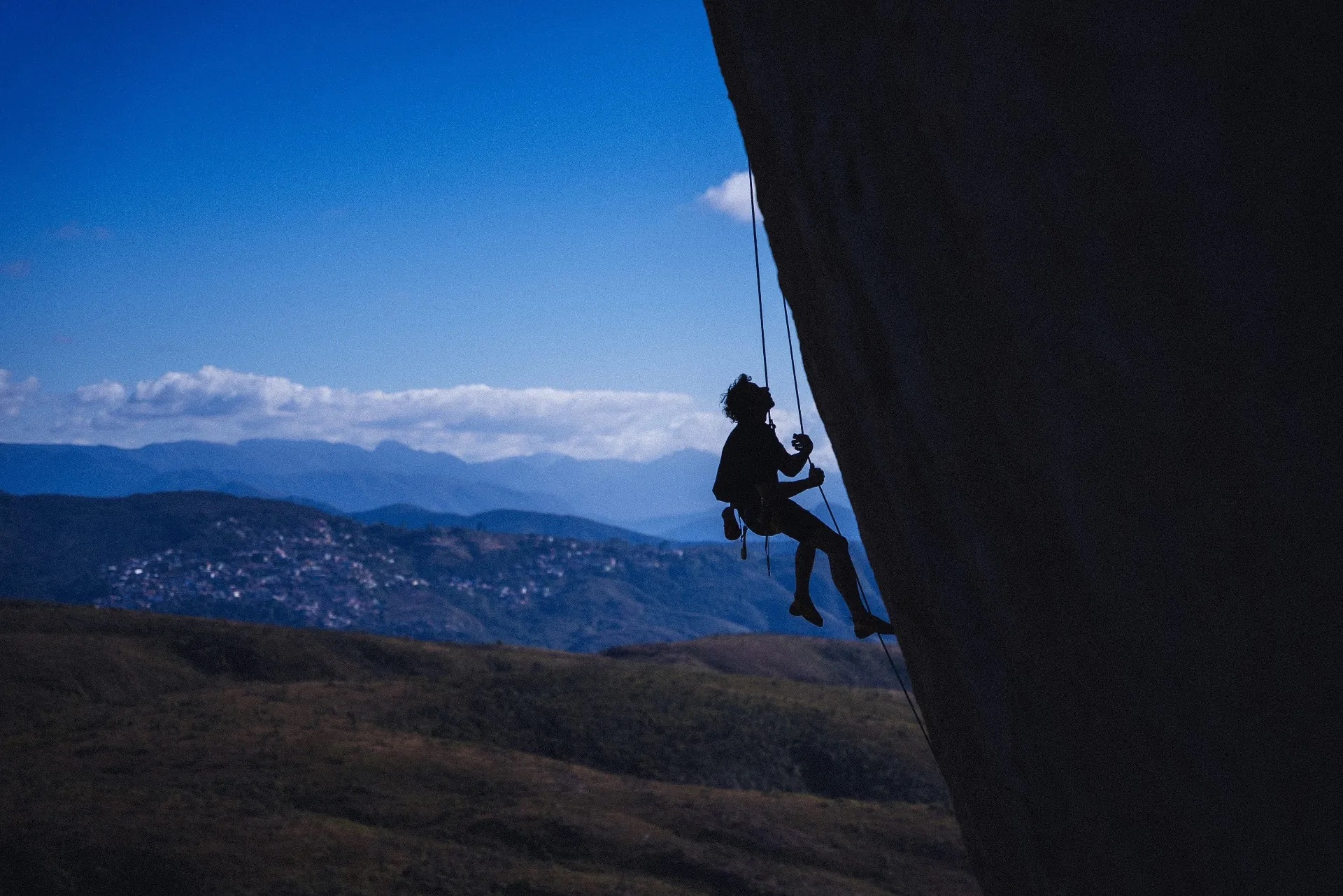 Escalador pendurado na rocha contra o céu azul